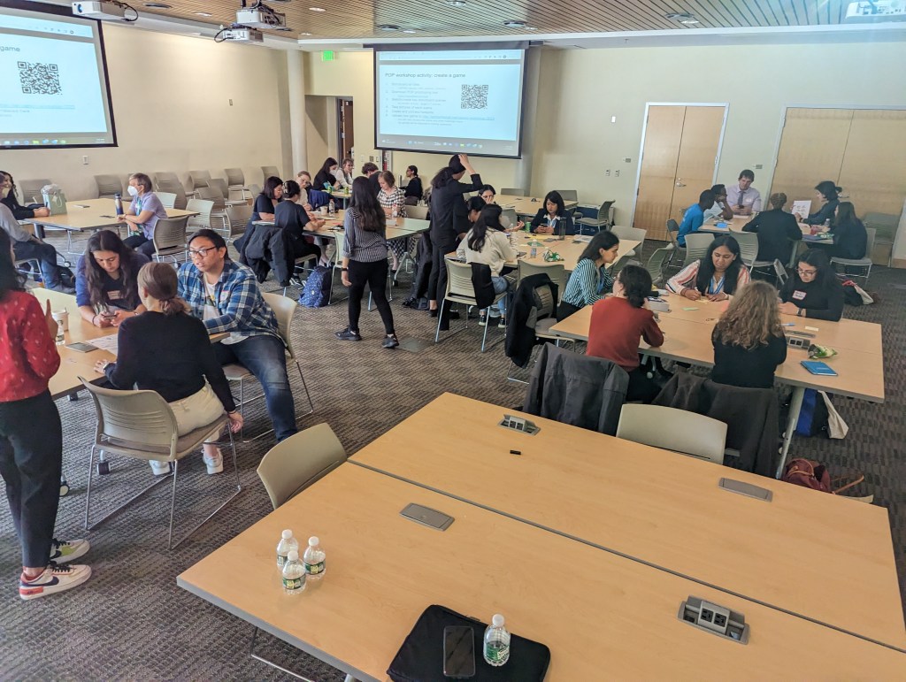 Workshop teams work on their game designs, as workshop co-organizers Morva Saaty and Jaitun Patel offer suggestions and technical advice